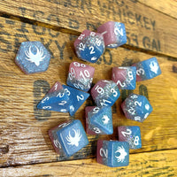 Set of blue and pink dice with white numbers and symbols on a wooden surface.