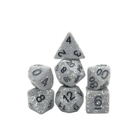 A set of seven silver glitter polyhedral gaming dice with black printed numbers, arranged on a plain white background.