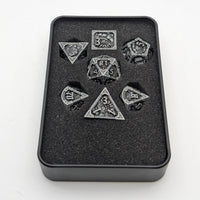 Set of metallic dice with intricate designs in a black box on a white background